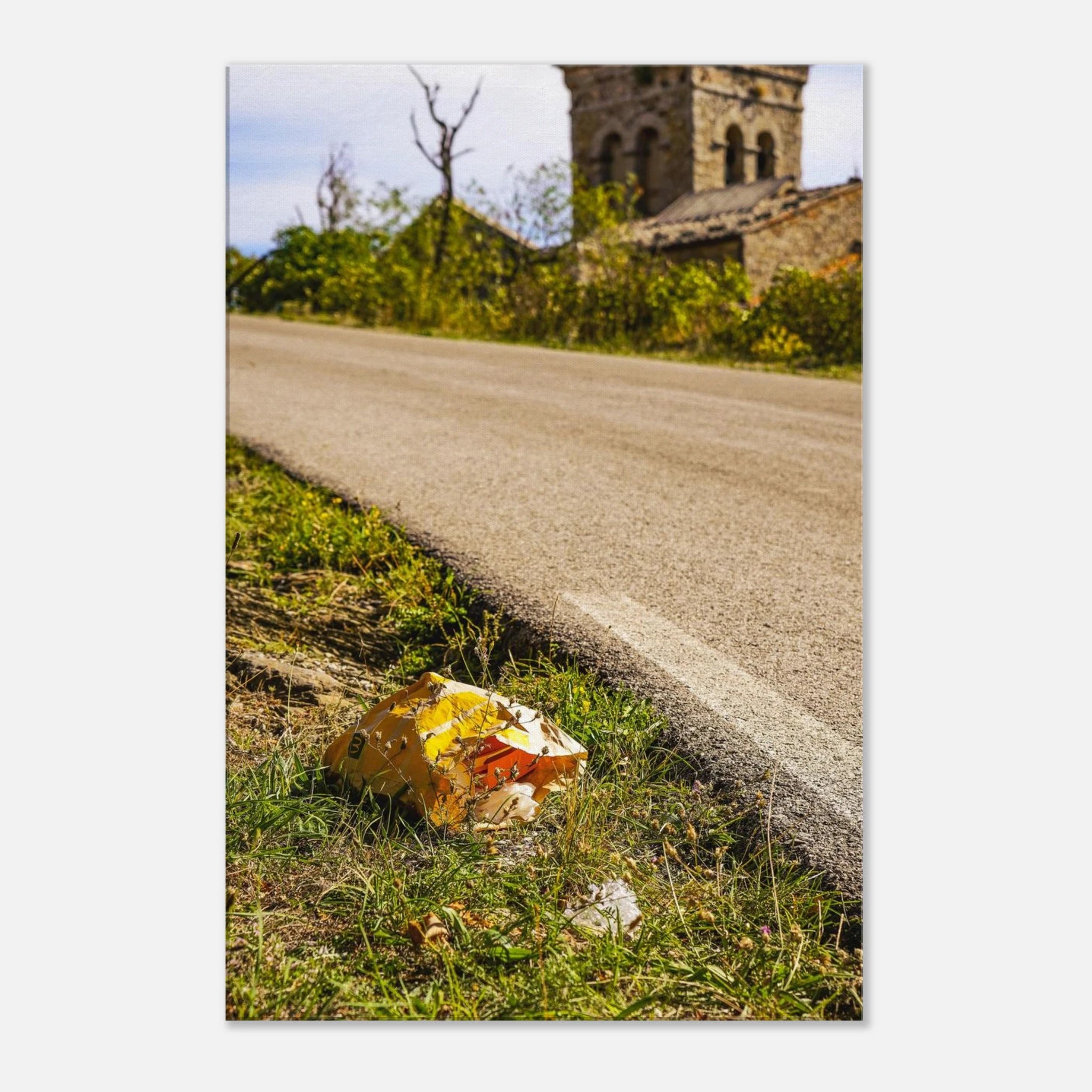 A discarded McDonalds bag sits in the grass beside a small road with a beautiful Italian church in the background.